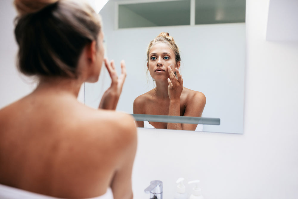 Girl looking into a mirror as she applies skin cream
